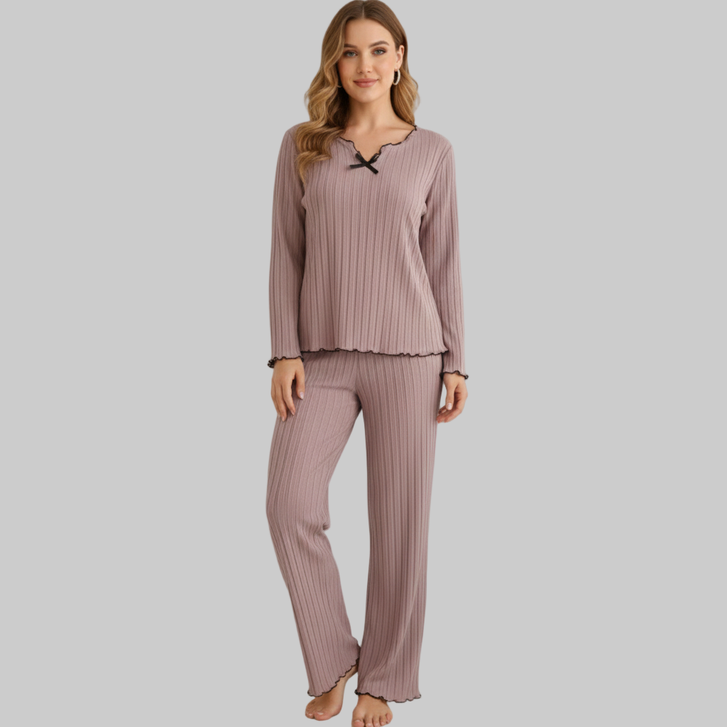 Kobieta ubrana w fioletowy, prążkowany zestaw domowy z długimi rękawami i czarnymi wykończeniami, stojąca boso na szarym tle.