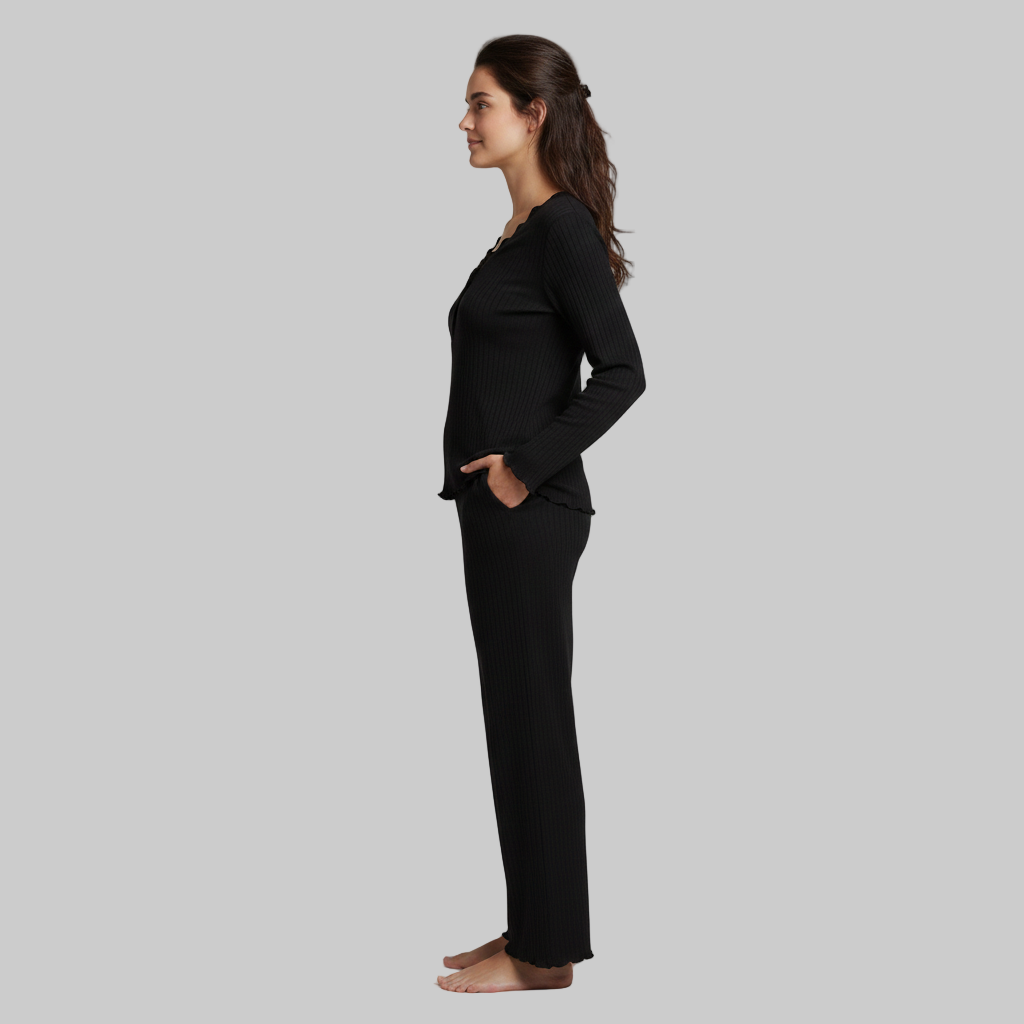 Kobieta ubrana w czarny zestaw domowy z prążkowanej dzianiny, widok z profilu przedstawiający luźne rękawy i spodnie z szerokimi nogawkami na szarym tle.
